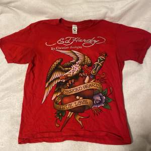 Säljer en cool röd t-shirt från Ed Hardy med ett stort tryck av en örn och ett hjärta med texten 'Pierced Hearts True Love'. T-shirten är kortärmad och har märkets logga både fram och bak. Använt den Max 2 gånger, jätte bra skick! Skulle säga att den är S/M, den är lite mer åt det oversized hållet.