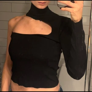 Svart oneshoulder polotopp - Säljer en stilren svart oneshoulder polotopp med lång ärm på ena sidan. Toppen skick! 