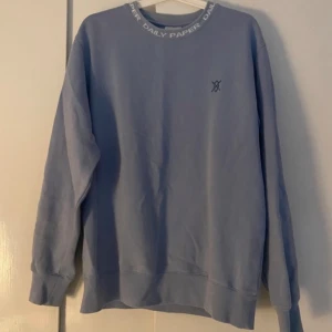 Ljusblå tröja från Daily Paper - Säljer en ljusblå tröja från Daily Paper. Den har en broderad logga på bröstet och text på kragen. Tröjan är i bra skick förutom att den har en väldigt svag fläck på magen som syns på bild 3.