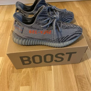 Adidas Yeezy Boost 350 V2 Beluga 2.0 - Säljer ett par Adidas Yeezy Boost 350 V2 i grått med orange detaljer. Skorna är i nytt skick och har en cool, stickad design med snörning. Perfekta för både vardag och fest! Kommer i originalförpackning.