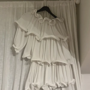 Vit klänning med volanger från NA-KD - Säljer en superfin vit klänning från NA-KD i storlek 34. Den har massor av volanger som ger en härlig och lekfull look. Perfekt för sommarens fester eller en speciell dag. Klänningen är axelbandslös och har en luftig passform. 🌸