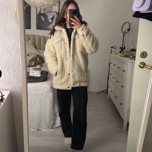 Beige teddyjacka från Monki - Mysig beige teddyjacka från Monki i storlek XS. Perfekt för kyliga dagar med sitt fluffiga material och bekväma passform. Jackan har knappar framtill och är långärmad, vilket gör den idealisk för höst och vinter. Superfin att ha både till vardags och när du vill mysa till det lite extra! 🧥✨