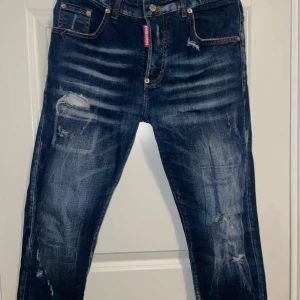 Blå jeans från Dsquared2 - Säljer ett par snygga blå jeans från Dsquared2 i bra skick. De har en cool slitningseffekt och klassisk femficksdesign. Perfekta för en avslappnad stil med en touch av edge. Passar både till vardags och fest! Byxorna är äkta!  
