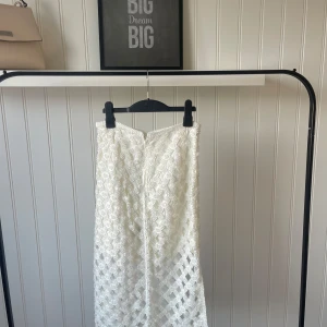 Vit spetskjol - Säljer en superfin vit spetskjol i mycket bra skick. Kjolen har ett vackert mönster med blommiga detaljer och är perfekt för sommarens alla fester. Den är knälång och har en elegant passform som passar både till vardags och festligare tillfällen.