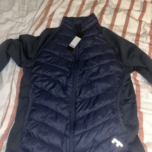 Mörkblå pufferjacka från 157 - Säljer en snygg mörkblå pufferjacka från 157 i storlek S. Jackan har en dragkedja framtill och är i mycket bra skick. Perfekt för höst och vår med sin quiltade design och långa ärmar. Den är både stilren och praktisk för kyligare dagar.