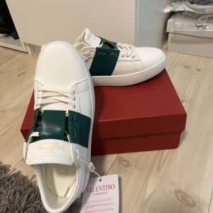 Valentino open - Säljer ett par snygga Valentino Garavani sneakers i vitt och grönt. Skorna är i nytt skick och kommer med originalförpackning och dustbag. Perfekta för både vardag och fest med sin stilrena design och högkvalitativa material.