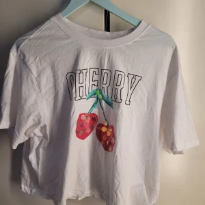 Vit t-shirt med körsbärstryck från ONLY - Säljer en superfin vit t-shirt från ONLY i storlek S. Den har ett coolt körsbärstryck med texten 'CHERRY' på framsidan. Perfekt för sommardagar eller en avslappnad look. T-shirten är kortärmad och i bomull, vilket gör den skön och luftig att ha på sig. 🥰
