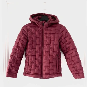 Vinröd bubbeljacka från Everest - Säljer en snygg vinröd bubbeljacka från Everest. Jackan är perfekt för kyliga dagar med sitt quiltade mönster och mysiga huva. Den har en dragkedja framtill och är tillverkad i 100% polyamid med fyllning av polyester. Perfekt för höst och vinter!