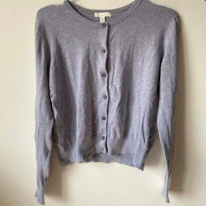 Grå kofta från H&M - Säljer en stilren och enkel grå kofta från H&M Basics. Den är långärmad och har knappar framtill. Perfekt för både vardag och lite kyligare dagar. Koftan är i ett mjukt material som känns skönt mot huden.