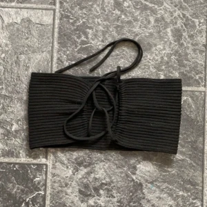 Svart ribbad bikiniöverdel - Säljer en snygg svart topp i ribbat material. Den har en stilren design med knytning fram som ger en extra touch. Perfekt för sommarens alla äventyr! Det går att välja lite hur man vill hur toppen ska sitta. Toppen är väldig stretchig.