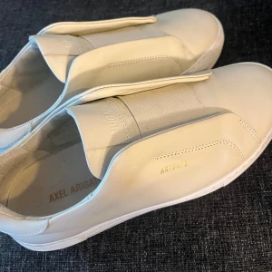 Axel arigato skor - jag säljer ett par Axel Arigato skor beige som används 1 gång, nytt skick, man får me allt, arigato påsen och boxen som man fick med. Storlek 40, nypris 2500 säljer för 1500