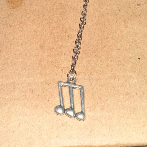 Halsband med musiknot i silver - Säljer ett snyggt halsband med en hängande musiknot i silverfärg. Kedjan är tunn och elegant, perfekt för musikälskare som vill ha något unikt och stilrent. Passar både till vardags och fest!