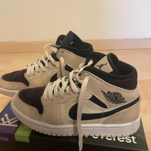 Nike Air Jordans i beige och svart - Snygga Nike Air Jordans i beige och svart med klassisk snörning och ikonisk Air Jordan-logga på sidan. Perfekta för en stilren look.