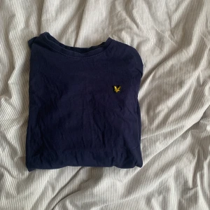 Mörkblå tröja från Lyle & Scott - Säljer en mörkblå tröja från Lyle & Scott med deras ikoniska gula logotyp på bröstet. Perfekt för en stilren och avslappnad look. Passar ungdomar i åldern 14-15 år.