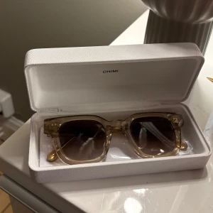 Transparenta solglasögon från Chimi - Snygga transparenta solglasögon från Chimi med fyrkantig form. De har en stilren design och kommer i ett elegant fodral. Perfekta för soliga dagar och ger en trendig look. Färgen ecru