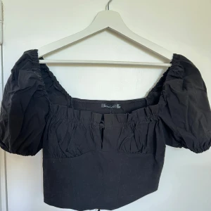 Svart kortärmad topp från Boohoo - Snygg svart topp från Boohoo med puffiga korta ärmar och en fyrkantig urringning. Toppen har en croppad passform och elastiska detaljer vid ärmslut och midja för en bekväm känsla.