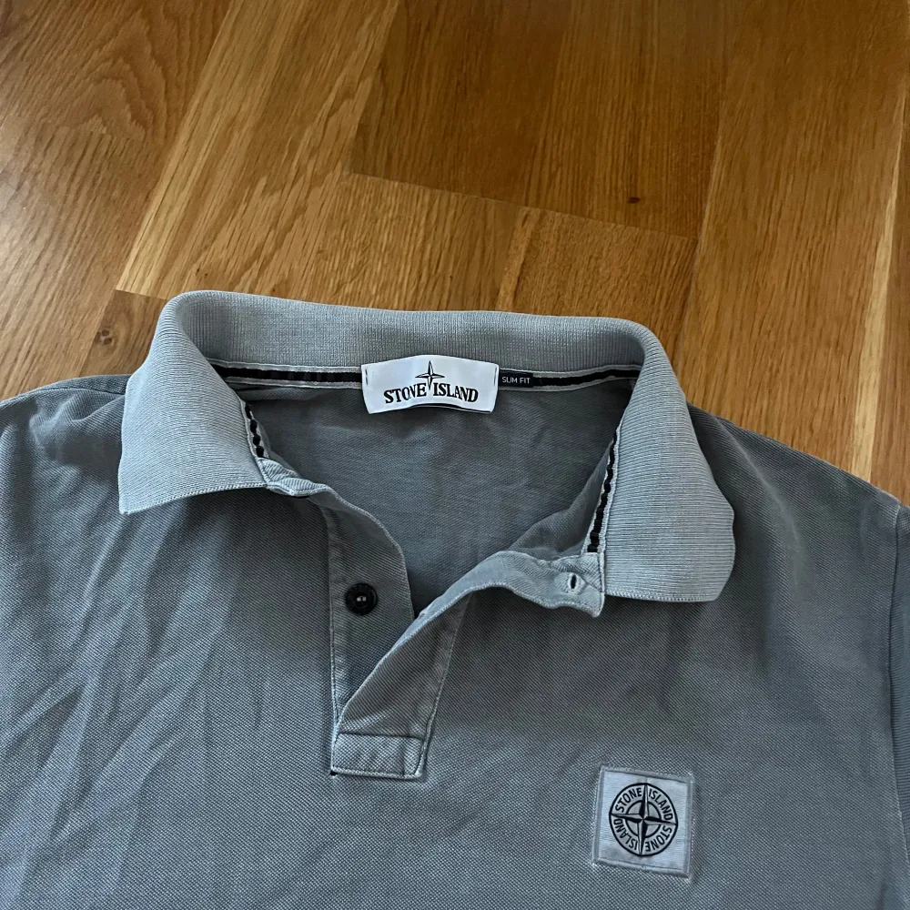 grå pikétröja från Stone Island med korta ärmar och klassisk krage. Tröjan har en broderad logotyp på bröstet och knappar vid halsen. Perfekt för en avslappnad men snygg look. Storlek på tröja är XL men killen på bilden bär M i allt och är 180cm tror den har krympt . T-paidat.