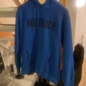 Blå hoodie från Hoodrich - Säljer en snygg och bekväm blå hoodie från Hoodrich med svart text på bröstet. Den har en klassisk känguruficka och justerbar huva med dragskott. Hoodien är original och köpt från JD för 750kr men säljer den för 350kr. Inga fläckar, hål eller slitage – väl omhändertagen!