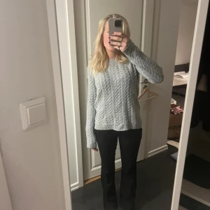 Grå stickad tröja från Crocker - Säljer en mysig grå stickad tröja från Crocker med flätmönster. Tröjan har långa ärmar och ribbstickade muddar vid ärmslut och nederkant. Perfekt för kyliga dagar!