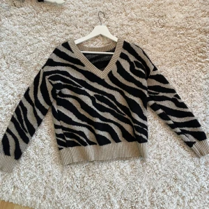 Zebramönstrad tröja från Vila - Säljer en snygg zebramönstrad tröja från Vila i svart och beige. Tröjan har en v-ringad hals och långa ärmar med ribbade muddar. Väldigt mjukt material! 