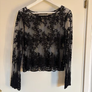 Svart spetsblus - Elegant svart spetsblus med långärmad design och vackra blommiga detaljer. Perfekt för en stilfull look med transparent material som ger en sofistikerad touch. Använd vid endast ett tillfälle :)