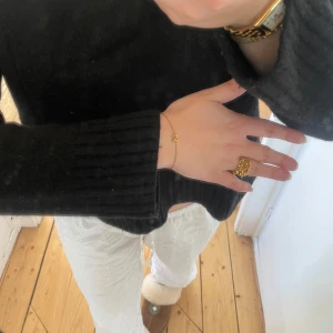 Svart stickad tröja - Säljer en svart stickad tröja med långa ärmar och ribbade detaljer vid ärmsluten. Tröjan har en croppad passform som ger en modern look. Perfekt för kyligare dagar.