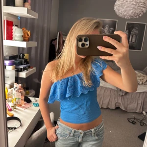 Blå ondshoulder topp med volang - Snygg blå offshoulder topp med volangdetaljer. Perfekt för sommardagar och ger en fräsch look. Toppen är croppad och har en luftig passform. Man kan ha den på tre olika sätt och den är i bra skick 