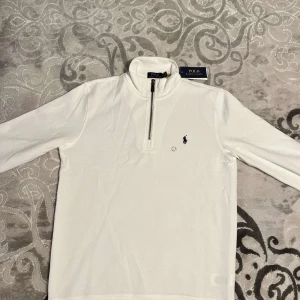 Polo Ralph Lauren Half-Zip - Snygg vit tröja från Polo Ralph Lauren med halv dragkedja och klassisk logga på bröstet. Perfekt för en stilren look. Helt felfri och aldrig använd!