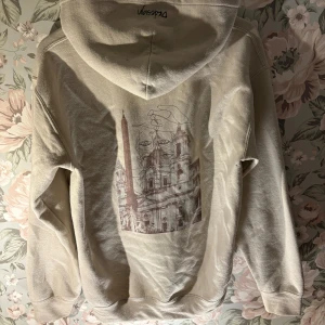Beige hoodie med tryck - Säljer en beige hoodie med en unik tryckdesign på baksidan. Tröjan har en klassisk känguruficka och en bekväm huva. Perfekt för en avslappnad stil. 
