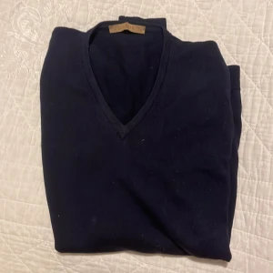 Mörkblå tröja från John Barritt - Säljer en stilren mörkblå tröja från John Barritt med v-ringning. Perfekt för en klassisk look. Tröjan är mjuk och bekväm, idealisk för kyligare dagar.