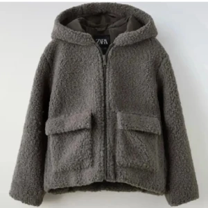 Grå teddyjacka från Zara - Mysig grå teddyjacka från Zara med huva och dragkedja. Jackan har två stora fickor framtill och är perfekt för kyliga dagar. Den har en avslappnad passform och är superbekväm att bära.💕Storleken är 164 i barnstorlek men uppskattas som S🥰