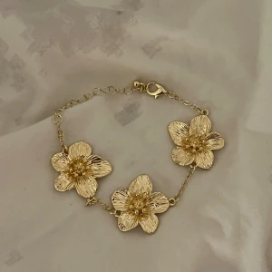 Guld blommigt armband  - Superfint guldigt armband med blommor från åhléns som är justerbart och helt nytt💕