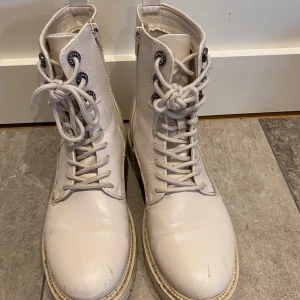 Beige boots med snörning - Snygga beige boots med snörning och dragkedja på sidan. Perfekta för höst och vår, dessa boots har en stilren design med rund tå och robust sula. Små skavmärken på tårna.