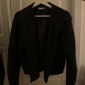 Svart kappa från Design by Si - Elegant svart jacka från Design by Si med klassisk design. Perfekt för en stilren look. Kappan passar till många tillfällen och är använd av mig ca 3 gånger. Jag säljer för att jag har köpt en ny som är i mörkblå och kappan är alltså nästan helt ny😊 Det är lite vitt ludd på den som man ser på sista bilden men det går att ta bort 🤗