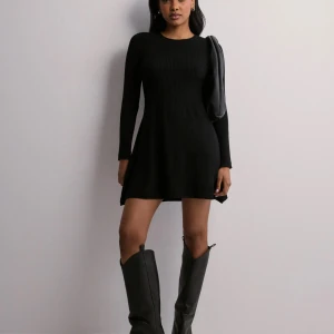 Svart ribbad klänning från Only M - Snygg svart ribbad klänning från Only med långärmad design. Perfekt för en stilren look, med en kort längd som ger en modern touch. Klänningen har en rund hals och är tillverkad i ett bekvämt material.