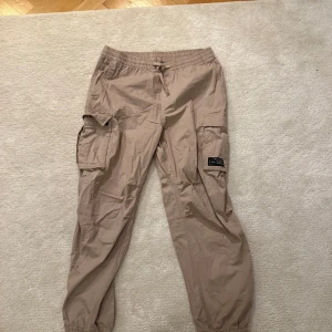Beige cargobyxor med snörning - Snygga beige cargobyxor med elastisk midja och snörning. Baggy fit. Storlek M. Byxan är i väldigt bra skick och är knappt använd.