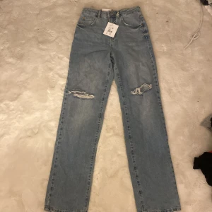 Ljusa jeans med slitningar - Snygga ljusblå jeans med slitningar på knäna. De har en klassisk femficksdesign och är högmidjade för en bekväm passform. Perfekta för en avslappnad stil. Nya med prislapp