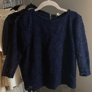 Mörkblå spetsblus - Säljer en elegant mörkblå spetsblus med trekvartsärm och rund hals. Perfekt för en stilren look med dragkedja i ryggen för enkel påklädning.