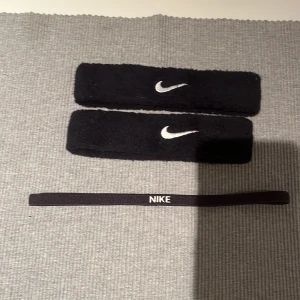 Svart diadem och svettband från Nike - Snyggt set med svart diadem och två svettband från Nike. Diademet är smalt med vit logga, perfekt för träning. Svettbanden är breda och mjuka med vit Nike-logga, idealiska för att hålla svetten eller håret borta under tränningspasset