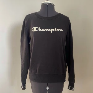 Svart sweatshirt från Champion - Svart sweatshirt från Champion med deras logga i vitt på bröstet och ärmen. Tröjan har långa ärmar och ribbade muddar.