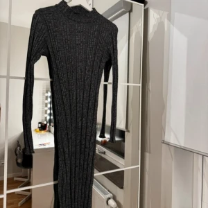 Grå ribbad klänning - Snygg grå ribbad klänning med lång ärm och hög krage. Perfekt för kyligare dagar med sin stickade look. Klänningen har en figurnära passform som framhäver silhuetten.