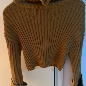 Brun ribbad stickad tröja från Fullamoda - Säljer en snygg brun ribbad stickad tröja från Fullamoda. Tröjan är croppad med långa ärmar och en mysig polokrage. Perfekt för kyliga dagar!