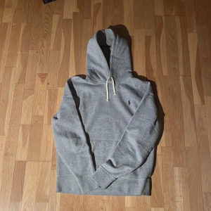 Grå hoodie från Polo Ralph Lauren - Säljer en stilren grå hoodie från Polo Ralph Lauren med klassisk logga på bröstet. 