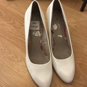 Vita pumps från Tamaris - Säljer ett par eleganta vita pumps från Tamaris i storlek 40. Skorna har en klassisk design med spetsig tå och klack, perfekt för en stilren look. Insidan har ett färgglatt mönster som ger en extra touch.