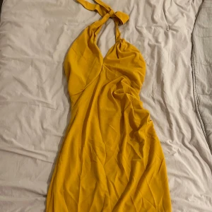 Gul klänning med halterneck - Helt ny snygg gul klänning med halterneck-design och draperad detalj framtill. Klänningen har en slits baktill som ger extra rörelsefrihet. Perfekt för en somrig look! Midiklänning! Storlek M. 