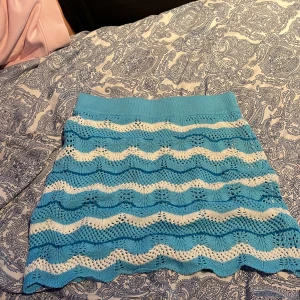 Blå och vit stickad kjol från FB Sister - Säljer en söt stickad kjol från FB Sister i blått och vitt med vågigt mönster. Kjolen har en elastisk midja för bekväm passform. Perfekt för en avslappnad stil.