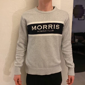 Stickad tröja Morris - Snygg grå tröja från Morris med texten 'Morris Rowing Club' i svart och vitt på bröstet. Passar även storlek L.      Modellen är 183 cm