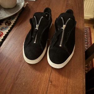 Axel Arigato skor med dragkedja  - Snygga svarta sneakers med dragkedja framtill och vit sula. Perfekta för en stilren look med enkel på- och avtagning. Passar bra till både jeans och mer avslappnade outfits. Man kan se att de är använde men allt de går att fixa !! Går att pruta!!