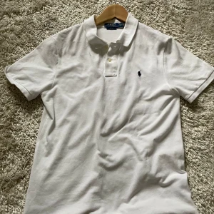 Vit pikétröja från Ralph Lauren - Säljer en klassisk vit pikétröja från Ralph Lauren i slim fit. Tröjan har korta ärmar och en liten broderad logga på bröstet. Perfekt för en stilren och avslappnad look. Passar både till vardags och fest!