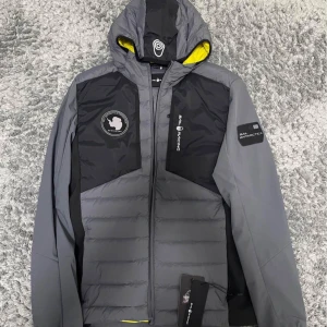 Sail Racing Antarctica Hybrid Hood - En helt ny och oanvänd Sail Racing Antarctica Hybrid Hood.  Storlek: Small  Färg: Mörkgrå med svarta detaljer Skick: Helt ny Pris kan diskuteras